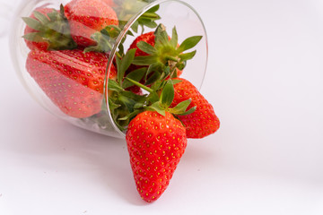 Close-up of a bunch of juicy strawberries in a lying wine glass on a white background