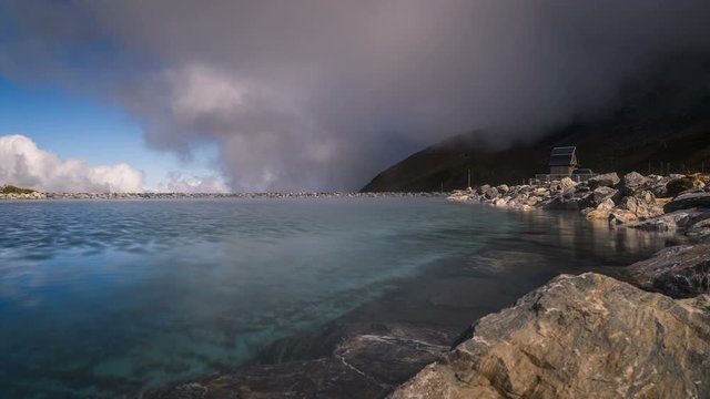 Motion time lapse of a rocky blue lake at Klein Scheidegg with mountains shrouded in misty clouds in the background in Grindelwald Switzerland.