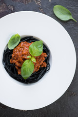 White plate with squid-ink spaghetti and bolognese sauce over brown stone background, vertical shot, view from above