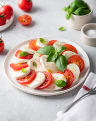 Italian caprese salad with sliced tomatoes, mozzarella, basil, olive oil on a light background. 