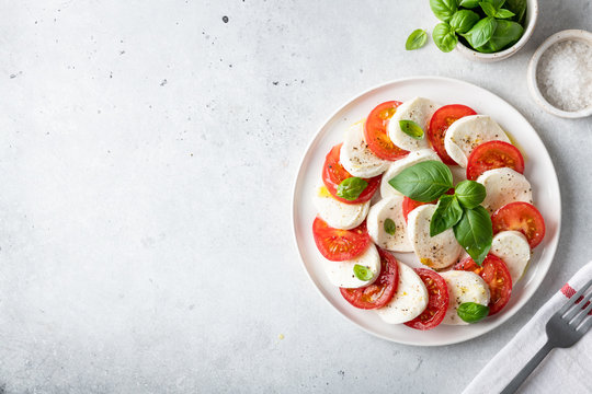 Italian caprese salad with sliced tomatoes, mozzarella, basil, olive oil on a light background. Top view, place for text.