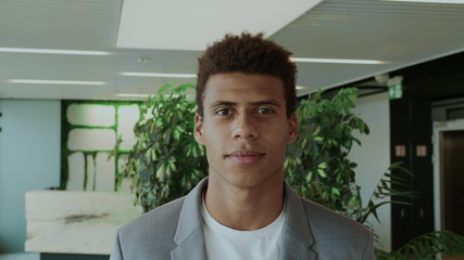 Fototapeta premium Young African-American man in elegant suit standing in modern office and smiling happily at camera.