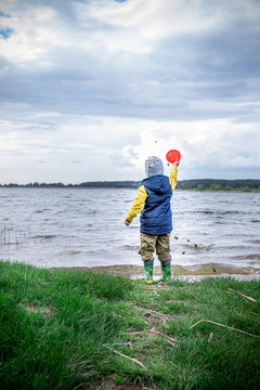 Little Kid Throwing Rocks In Lake. Rubber Boots