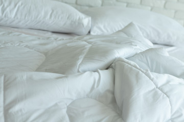 Messed bed with white pillow and blanket with natural light in bedroom in the morning,