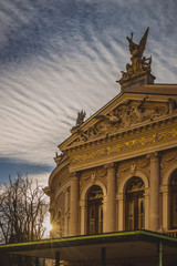 Beautiful opera house in Ljubljana, slovenia during sunset. Detail of the front facade with sun just sending rays of light at the side wall. Nice cloud texture above the house.