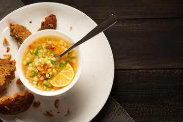 Italian soup with red lentils and small pasta - ptitim. Added vegetables, herbs and spices. On a plate lies brown bread with seeds. Copy space. Top view Flat lay. Rustic