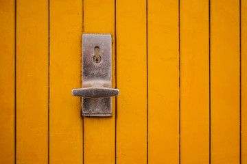 Metal handle and a lock on a garage door in yellow color. An older rusty metal knob with lock on a closed yellow garage door.