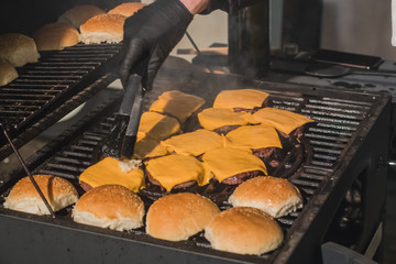 Preparing cheese burgers or hamburgers with bread buns on a hot coal grill outside. Detail of delitious juicy home made burgers.
