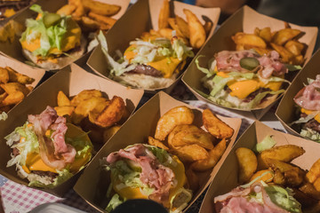 Preparing gourmet burgers or hamburgers with potatoes, bacon, cheese, buns. Detail of  half made burgers in cardboard boxes