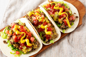 Homemade Cheeseburger Tacos on a rustic wooden board on a white wooden table, low angle view. Close-up.