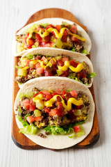 Homemade Cheeseburger Tacos on a rustic wooden board on a white wooden background, low angle view.