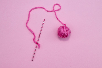 Crochet hook with a pink ball of wool on a pink background. Room for copy. 