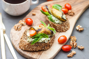 Bruschetta with grilled eggplant, cherry tomatoes, cheese dip, fresh basil and aromatic herbs. Mediterranean cuisine.