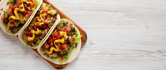 Homemade Cheeseburger Tacos on a rustic wooden board on a white wooden surface, top view. Flat lay, overhead, from above. Space for text.