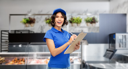mail service and shipment concept - happy smiling delivery girl in blue uniform with clipboard and pen writing over grocery store on background