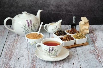 Obraz na płótnie Canvas Detail of a mug with red tea with a teapot, brown cane sugar and dry tea leaves