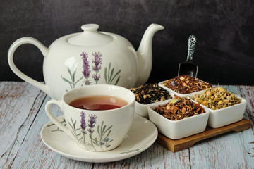 Mug with red tea, teapot and dry tea leaves. Dark background