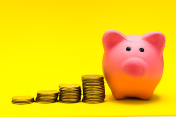 Pink piggy Bank on a yellow background, with a stack of coins showing growth. The concept of savings, financial management.