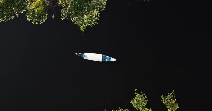 Aerial sinking shot with top down view of traditional wooden Shikara floating on silent Dal Lake in Kashmir, India.