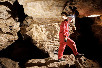 Man walking and exploring dark cave with light headlamp underground. Mysterious deep dark, explorer discovering mystery moody tunnel looking on rock wall inside.