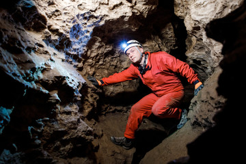 Man walking and exploring dark cave with light headlamp underground. Mysterious deep dark, explorer...