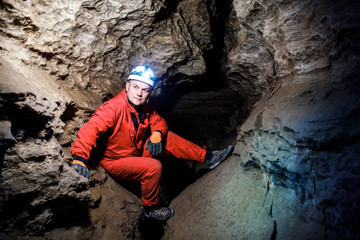 Man walking and exploring dark cave with light headlamp underground. Mysterious deep dark, explorer discovering mystery moody tunnel looking on rock wall inside.