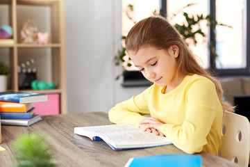 children, education and learning concept - little student girl reading book at home