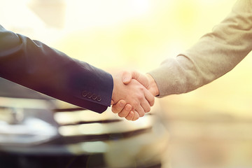Salesman shaking hands with customer in modern auto dealership, closeup. Buying new car