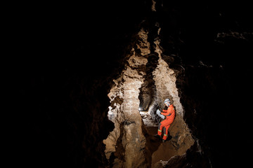Man walking and exploring dark cave with light headlamp and map in his hand underground. Mysterious deep dark, explorer discovering mystery moody tunnel looking on rock wall inside.