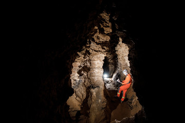 Man walking and exploring dark cave with light headlamp and map in his hand underground. Mysterious deep dark, explorer discovering mystery moody tunnel looking on rock wall inside.