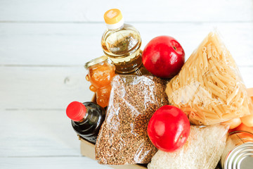 stock food at the isolation, the delivery of food in a crisis, coronavirus pandemic, food box on a white wooden background