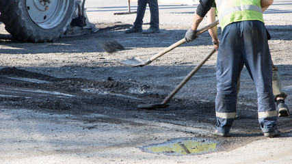 Road works. Workers repair the road surface and asphalt the street. People in overalls with shovels throw dirt and fill up holes in the road.