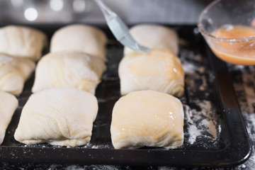Chef hand smearing samsa pasties with egg yolk before putting the pasties in the oven.