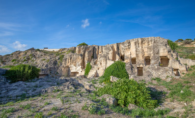 Fototapeta na wymiar Carved Limestone Rock Surrounded By Vegetation, The Punic Necropolis Of Tuvixeddu, Cagliari, Sardinia