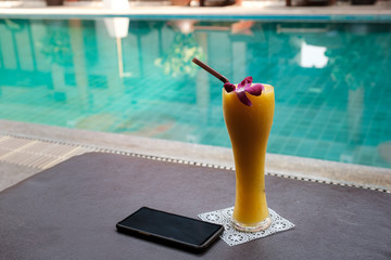 Mango smoothie with a smartphone on a sunbed against the background of the pool