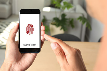 Man holding smartphone with fingerprint sensor indoors, closeup. Digital identity