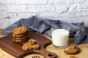 Oatmeal cookies with chocolate chips and cup of milk on kitchen table. Delicious oatmeal cookies on wooden board.