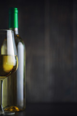 Transparent bottle of white dry wine on the table. White wine glass on a wooden background.