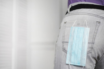 A disposable medical mask sticks out of a pocket instead of a napkin. A man with a disposable mask in a suit and jeans. Individual respiratory protection.