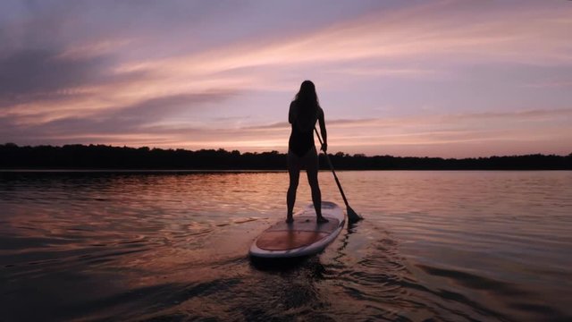 Girl stroking away on her stand up paddle board into the sunset