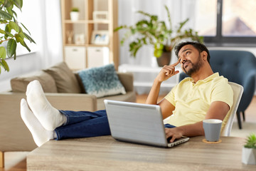 technology, remote job and lifestyle concept - indian man with laptop computer resting feet on table and thinking at home office
