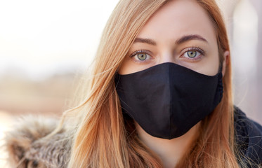 health, safety and pandemic concept - young woman wearing black face protective reusable barrier...