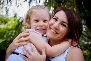 Happy mother and daughter resting and hugging in the park. Beauty nature scene with family outdoor lifestyle