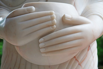 Close up of White marble Buddha sculpture or statue with two hands holding monk's alms-bowl in Buddhism religious temple for outdoor or indoor decoration   