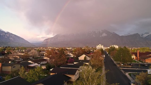 Flying up and over neighborhood towards rainbow after during storm moving over the mountains.