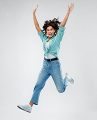 people, ethnicity and portrait concept - happy young woman in turquoise shirt and jeans jumping...