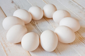 White chicken eggs lying on a white painted wooden surface. Background for livestock products.