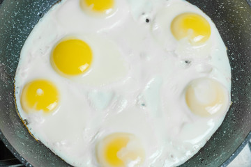 Six eggs in close-up frying in a pan on a gas stove, top view