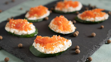 Sandwiches with cucumber at the base, cream cheese and salmon on top on a black tray. Healthy alternative