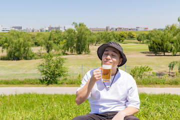 Fototapeta premium 屋外でビールを飲む日本人男性。青空背景